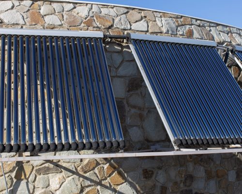 Solar water heating system installed on wall or roof of house. 3 panels of glass coaxial tubes with water to accumulate heat. Side view. Concept environmentally friendly and economical home heating.